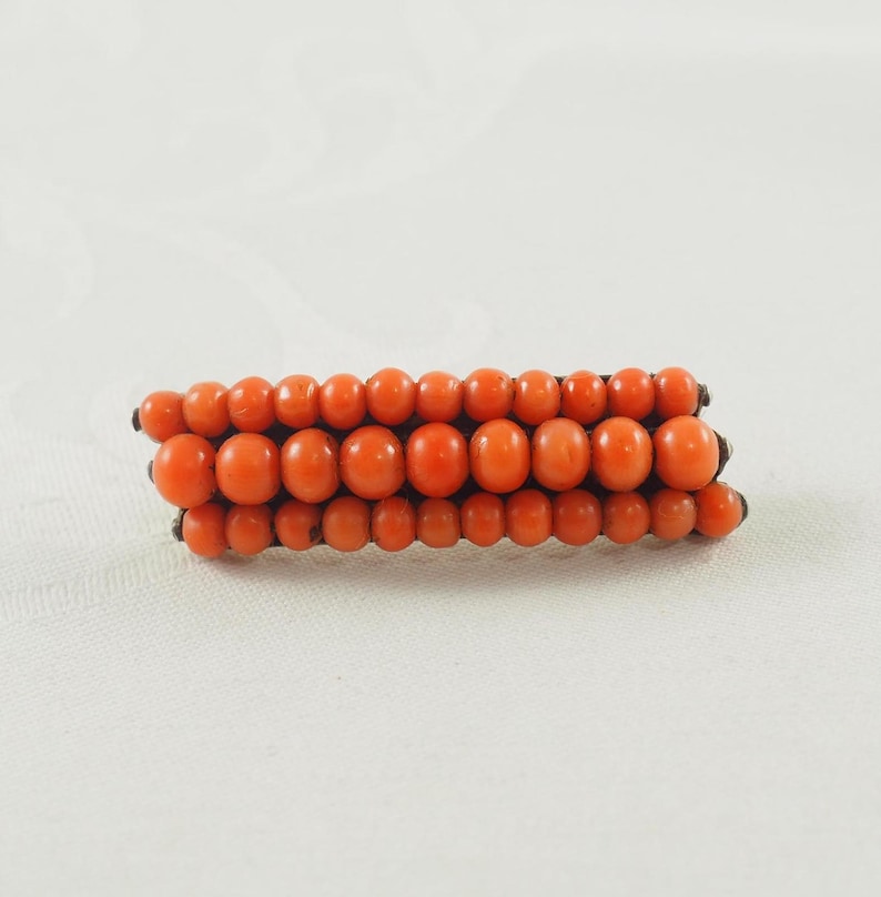 May include: A vintage brooch made of orange coral beads arranged in three rows.