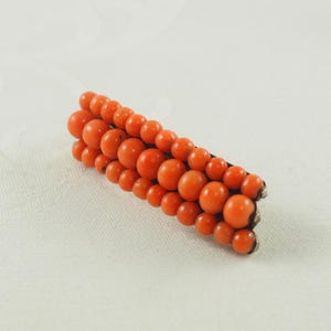 May include: A vintage brooch made of orange coral beads. The beads are arranged in a graduated pattern, with the largest beads at the center of the brooch. The brooch is set in silver.