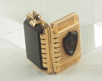 May include: A gold locket pendant with a black onyx cameo and a shield design. The locket is open and the cameo is visible.
