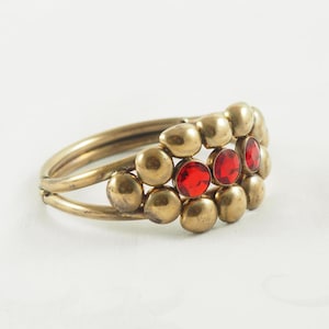 May include: A gold bangle bracelet with a cluster of round, gold beads and three red gemstones.