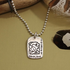 May include: A silver necklace with a silver tag pendant. The tag has a map design and the words "JOURNEY" and "PROV. 16:9" engraved on it.