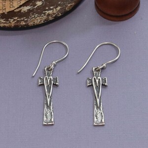 May include: A pair of silver dangle earrings with a cross design and a heart in the center. The cross is textured and the heart is smooth.