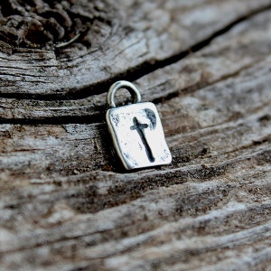 May include: A silver charm with a cross design. The charm is square shaped and has a loop at the top for attaching to a necklace or bracelet.