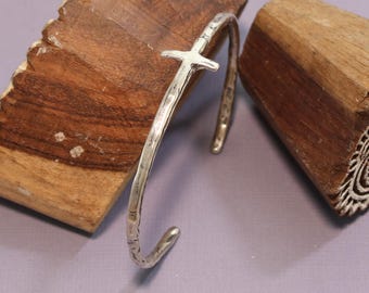 May include: A silver hammered cuff bracelet with a cross design. The bracelet is open and has a hammered finish.