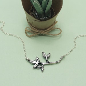 May include: A silver necklace with a delicate branch pendant featuring multiple leaves. The pendant is made of metal and has a natural, organic look.