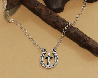Puede incluir: Un collar de plata con un colgante de herradura con una cruz y la palabra "blessed" inscrita en la herradura.