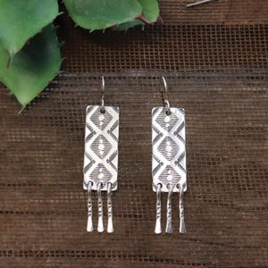 Peut inclure: Boucles d'oreilles pendantes en argent avec un motif géométrique et trois brins pendants.