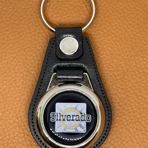 May include: Black leather keychain with a silver metal circle featuring the word "Silverado" in white lettering.