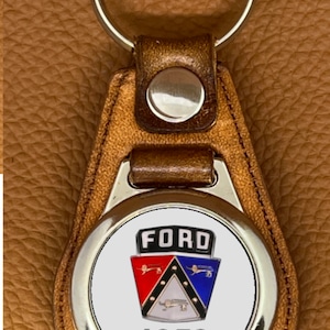 May include: A brown leather keychain with a silver metal circle featuring a vintage Ford logo and the year 1953.