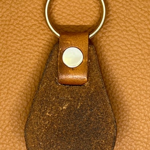 May include: A brown leather keychain with a silver key ring and a round, white button.