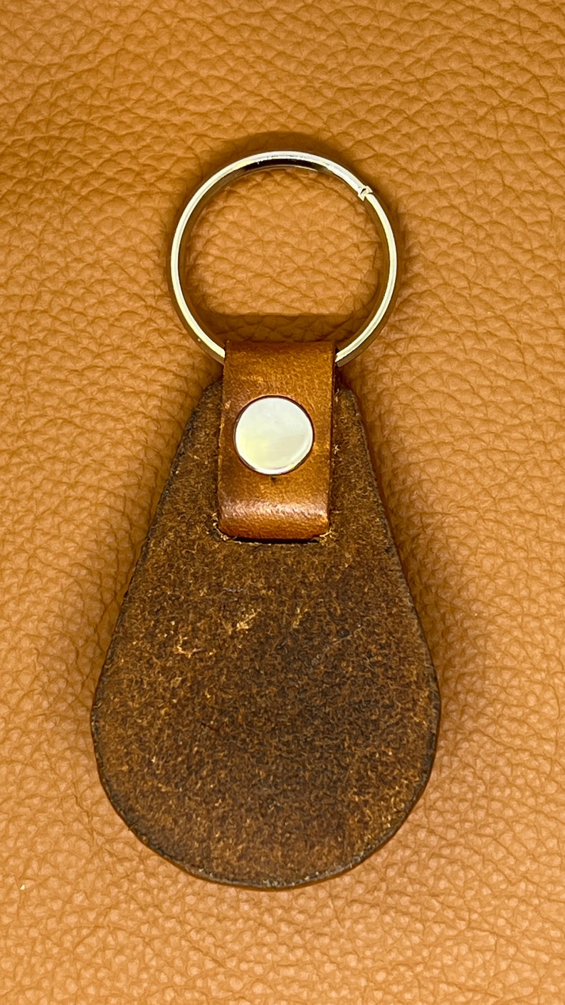 May include: A brown leather keychain with a silver key ring and a round, white button.