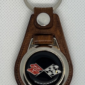 May include: Brown leather keyring with a silver metal ring and a round emblem featuring a red and white crossed flag design.