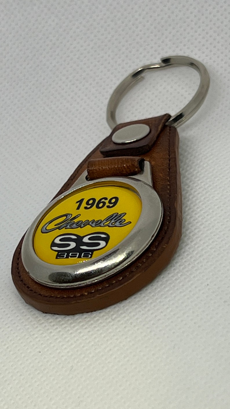 May include: A brown leather keychain with a silver metal charm. The charm features a yellow background with the text "1969 Chevelle SS 396".