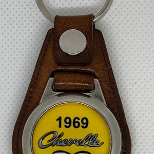 May include: A brown leather keychain with a silver metal ring and a round yellow emblem. The emblem features the text "1969 Chevelle SS 396" in black and silver lettering.