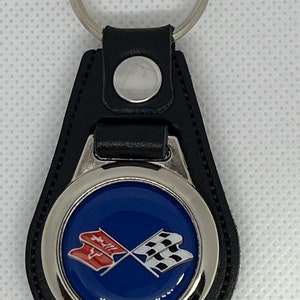 May include: A black leather keyring with a silver metal charm featuring a blue background with a red and white crossed flag design.
