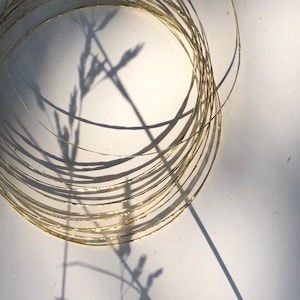 Peut inclure: Gros plan sur une pile de cercles de fil d'or, créant un motif circulaire. Le fil est texturé et a une finition brillante. Les cercles sont empilés les uns sur les autres, créant une impression de profondeur et de dimension.