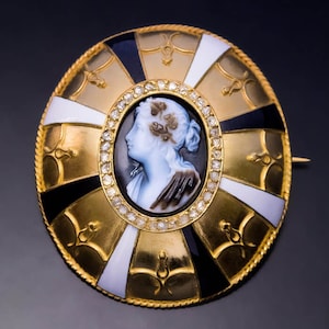 May include: A gold brooch with a cameo of a woman's profile set in a circle of diamonds. The brooch is decorated with black and white enamel and gold accents.