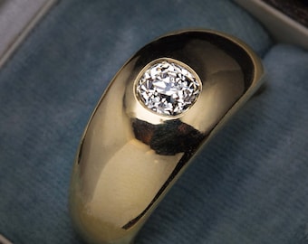 May include: A gold ring with a large, round, clear diamond set in the center. The ring is thick and has a rounded, domed top.