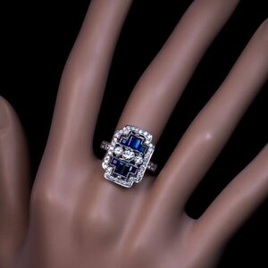 May include: A silver ring with a rectangular design featuring a cluster of blue sapphires and diamonds.
