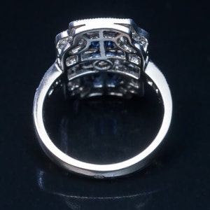 May include: A silver ring with a blue gemstone set in a square-shaped, intricate, diamond-like design.