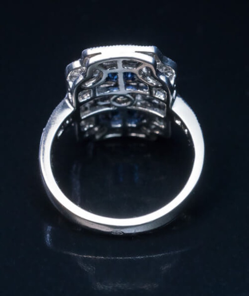 May include: A silver ring with a blue gemstone set in a square-shaped, intricate, diamond-like design.