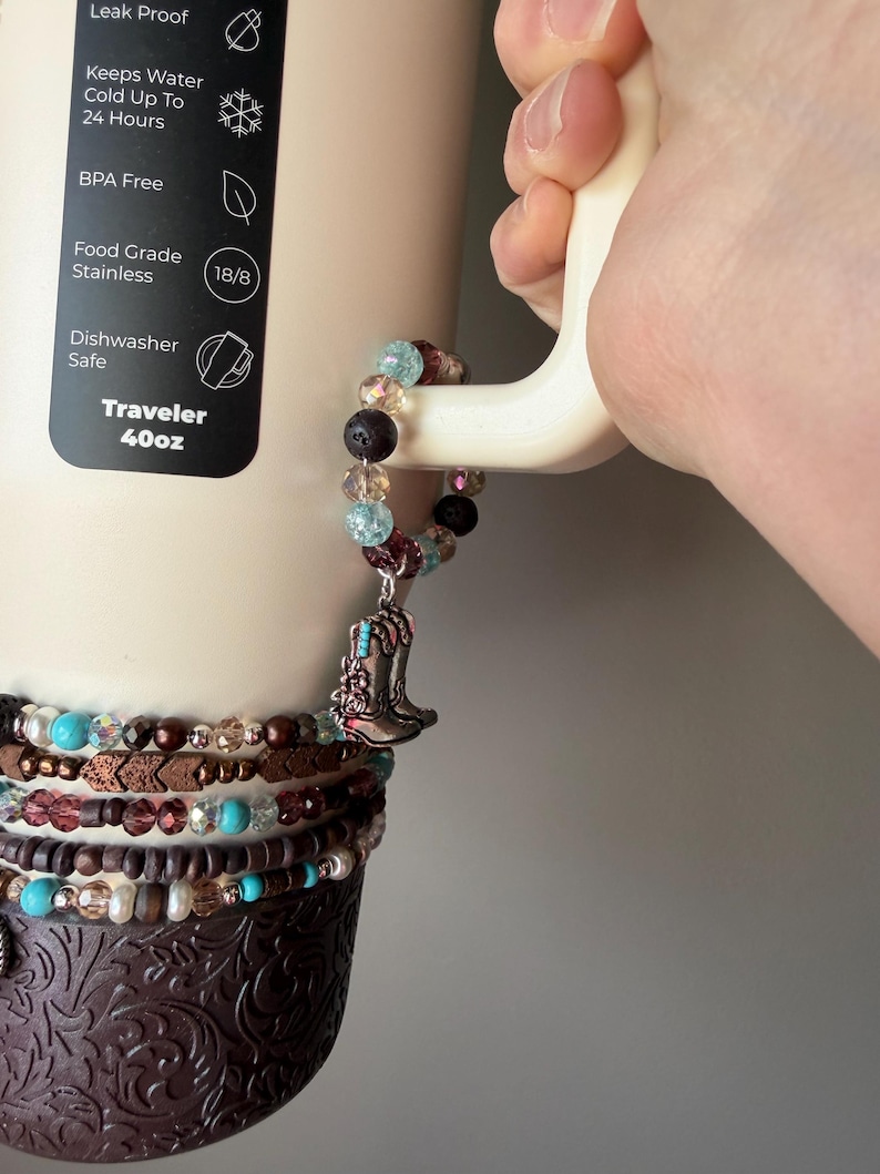 Puede incluir: Un vaso Traveler beige de 1,18L con una pulsera de cuentas decorativa y un dije de bota de vaquero plateada. El vaso tiene un dise&ntilde;o en relieve marr&oacute;n en la parte inferior e indica que es a prueba de fugas, sin BPA y apto para lavavajillas.