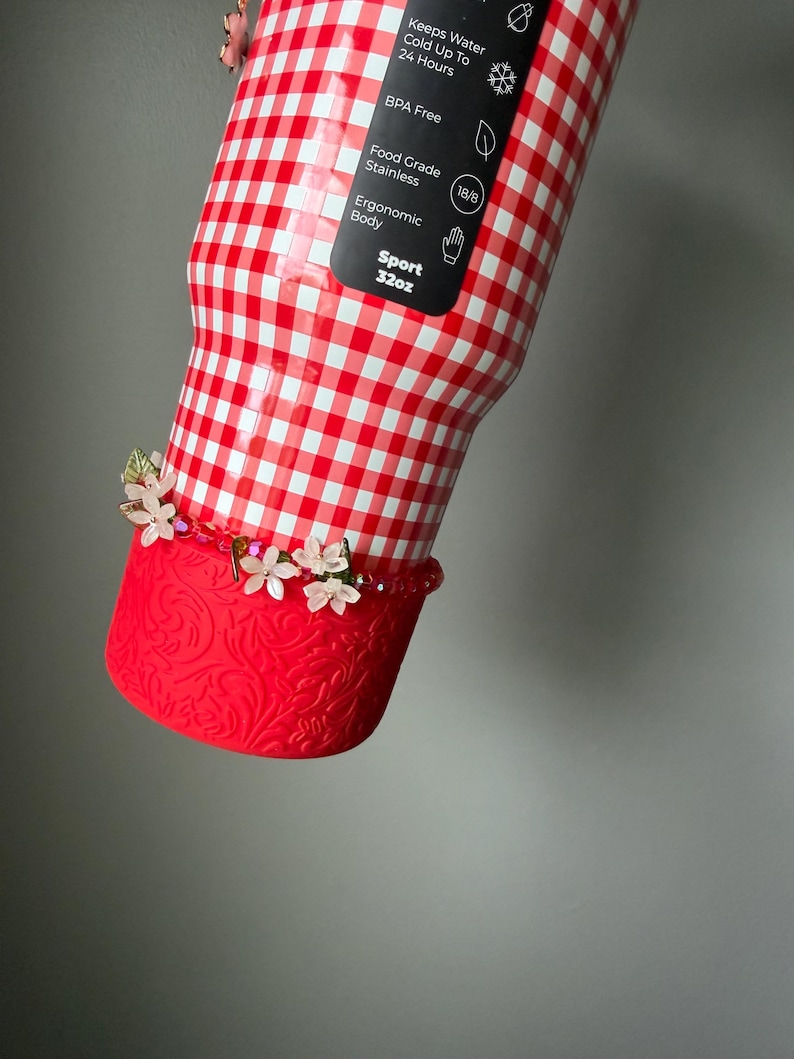 K&ouml;nnte beinhalten: Eine rot-wei&szlig; karierte Sportflasche mit roter Zierbasis. Die Flasche hat ein Fassungsverm&ouml;gen von 946 ml und eine florale Verzierung. Die Flasche besteht aus Edelstahl und ist BPA-frei.