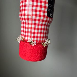 K&ouml;nnte beinhalten: Ein 946 ml Becher mit rot-wei&szlig;em Vichy-Muster. Der untere Teil ist rot mit einem floralen Design und mit kleinen wei&szlig;en Blumen verziert. Der Becher hat einen Sportk&ouml;rper und ist BPA-frei.
