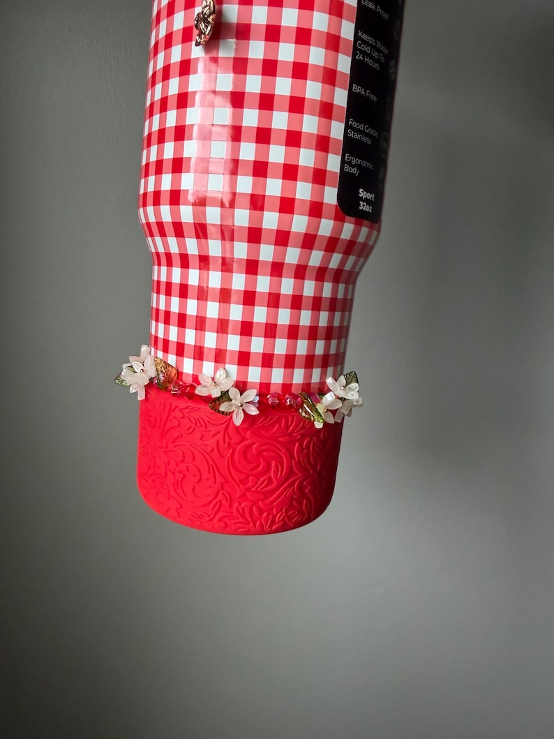 K&ouml;nnte beinhalten: Ein 946 ml Becher mit rot-wei&szlig;em Vichy-Muster. Der untere Teil ist rot mit einem floralen Design und mit kleinen wei&szlig;en Blumen verziert. Der Becher hat einen Sportk&ouml;rper und ist BPA-frei.