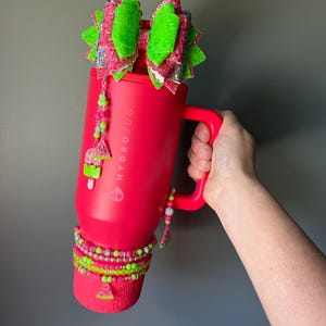 May include: A bright red HydroJug tumbler featuring a large, multi-layered glittery bow in neon green and pink attached to the lid. The tumbler is decorated with beaded charms, including watermelon slices, and a stack of matching neon beaded bracelets.