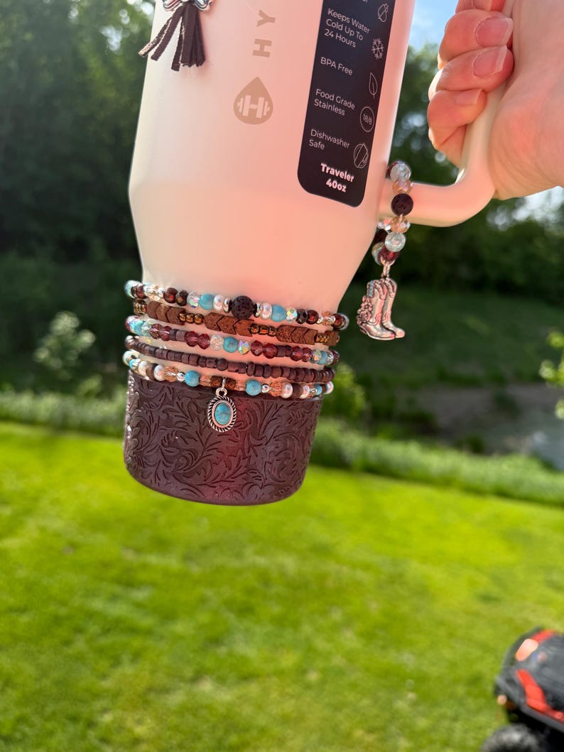 May include: A white 40oz Traveler water bottle with a brown patterned sleeve and multiple beaded bracelets. One bracelet has a turquoise pendant. A charm with a silver cowboy boot hangs from the handle.