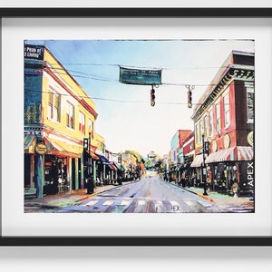 May include: A watercolour painting depicting a street scene in Apex, North Carolina. The street is lined with colourful buildings, some with awnings, and there are trees and a sign that reads "Welcome to Apex, The Peak of Good Living".