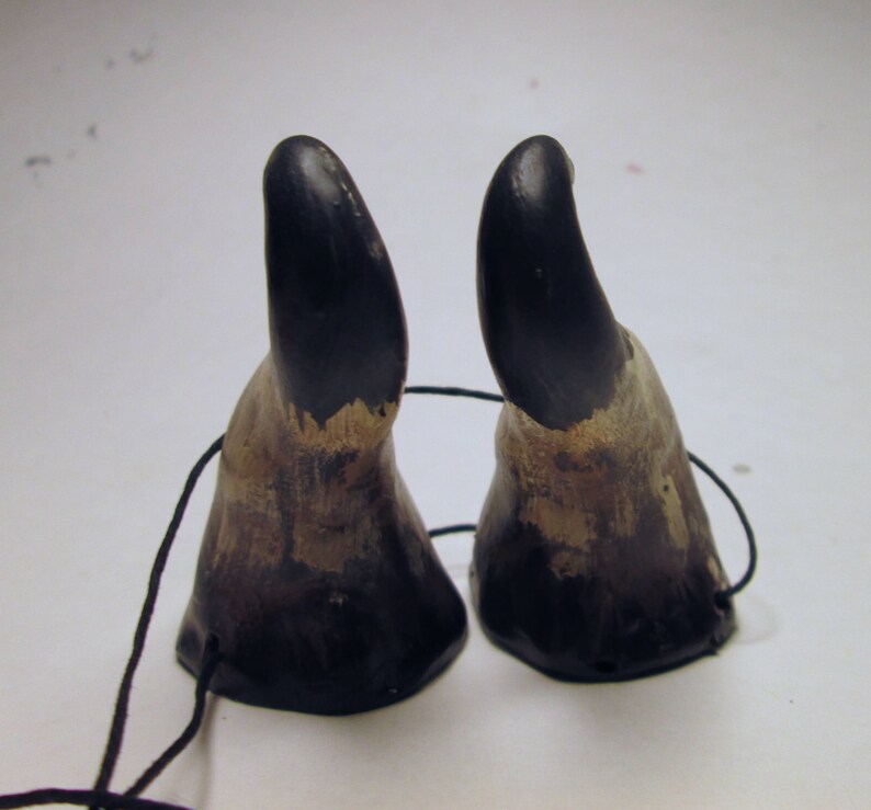 May include: Two black and brown animal horns with a black string attached to them.