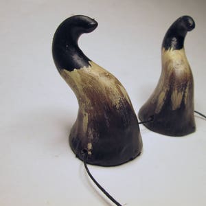 May include: A pair of black and brown horns with a black cord attached. The horns are made of a textured material and have a slightly curved shape.