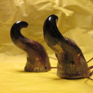 May include: Two black and purple horns with a gold and white paint design. The horns are made of a smooth, hard material and have a slightly curved shape.