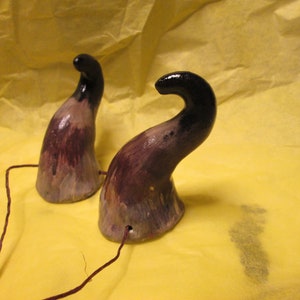 May include: Two ceramic horns painted in shades of brown, black, and white. The horns are attached to a thin brown string.