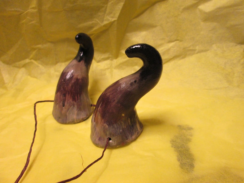 May include: Two ceramic horns painted in shades of brown, black, and white. The horns are attached to a thin brown string.