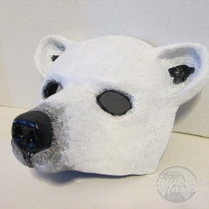 Puede incluir: M&aacute;scara de oso polar blanco con ojos y nariz negros. La m&aacute;scara est&aacute; hecha de papel mach&eacute; y tiene una superficie texturizada.