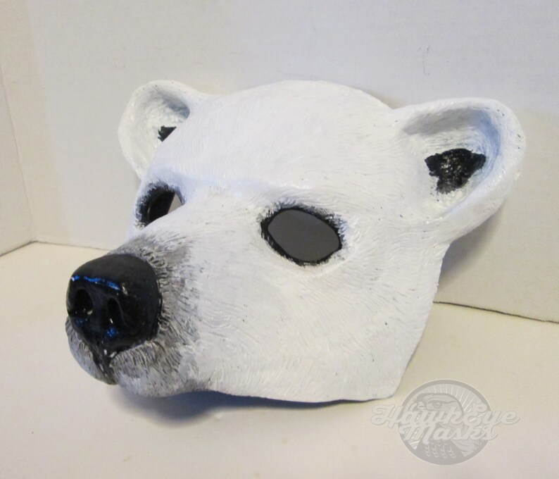 Puede incluir: M&aacute;scara de oso polar blanco con ojos y nariz negros. La m&aacute;scara est&aacute; hecha de papel mach&eacute; y tiene una superficie texturizada.