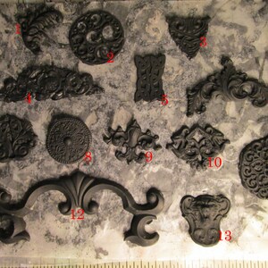 May include: A collection of black decorative resin embellishments, including ornate scrollwork, circular designs, and symmetrical shapes. The pieces vary in size and style, suitable for crafting or decorative projects.
