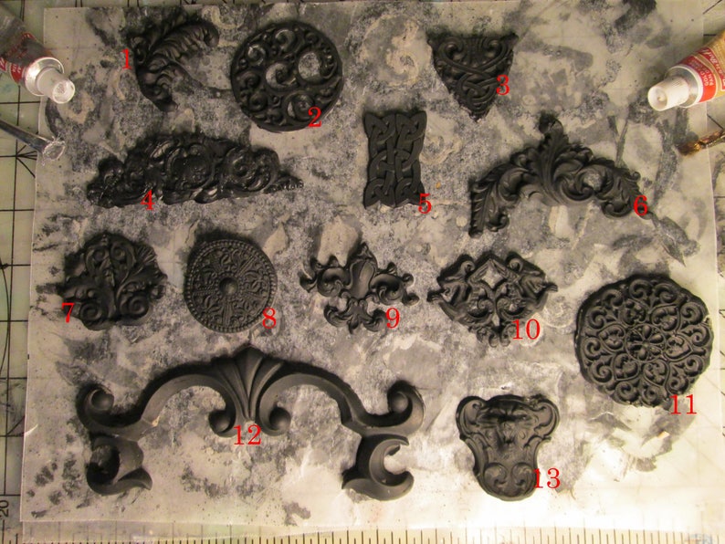 May include: A collection of black decorative resin embellishments, including ornate scrollwork, circular designs, and symmetrical shapes. The pieces vary in size and style, suitable for crafting or decorative projects.