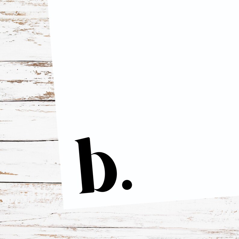 May include: A white background with the black letter "b" and a period. The letter is in a bold, serif font. The image is on a white wooden surface.