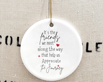 May include: A round white ceramic ornament hanging from a gold string. The ornament features black text that reads: It's the friends we meet along the way that help us Appreciate the Journey, accented with a small red heart and two red star icons.
