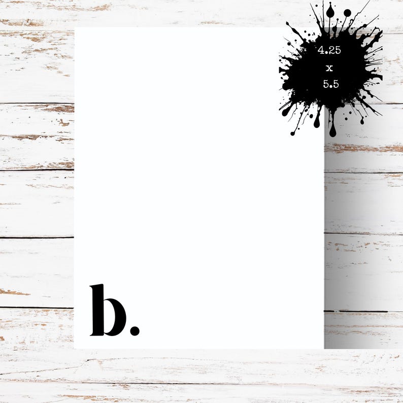 May include: A white rectangular card with the letter "b." in black at the bottom left corner. A black ink splatter with the text "4.25 x 5.5" is in the upper right corner. The background is a white wooden surface.