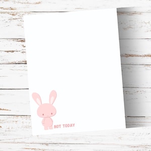 May include: A rectangular white sheet of paper featuring a small, light pink cartoon rabbit character positioned in the bottom left corner. Next to the rabbit, the text "NOT TODAY" is printed in a matching light pink, sans-serif font style.