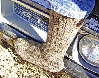 May include: A brown knitted sock with a textured pattern is worn on a person's foot. The sock is resting on the front bumper of a car with a black and silver grille. The grille has the letters "GT" printed on it.