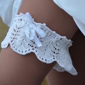 May include: White crocheted garter with a white satin bow. The garter is delicate and has a scalloped edge.