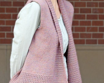 May include: A mauve knitted vest with a shawl collar. The vest features a textured bottom hem and is worn over a light green long-sleeved shirt. The background is a red brick wall.
