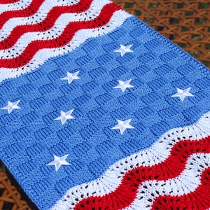 May include: A knitted baby blanket in red, white, and blue with a star pattern. The blanket is made with a chevron stitch and has a woven texture.