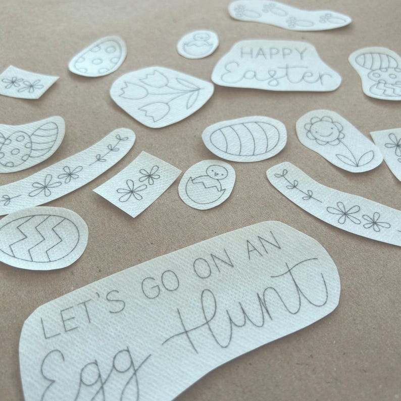 Pu&ograve; includere: Un set di ritagli di carta bianca con disegni a inchiostro nero di immagini a tema pasquale, tra cui uova, fiori, pulcini e il testo "Buona Pasqua" e "Andiamo a caccia di uova".
